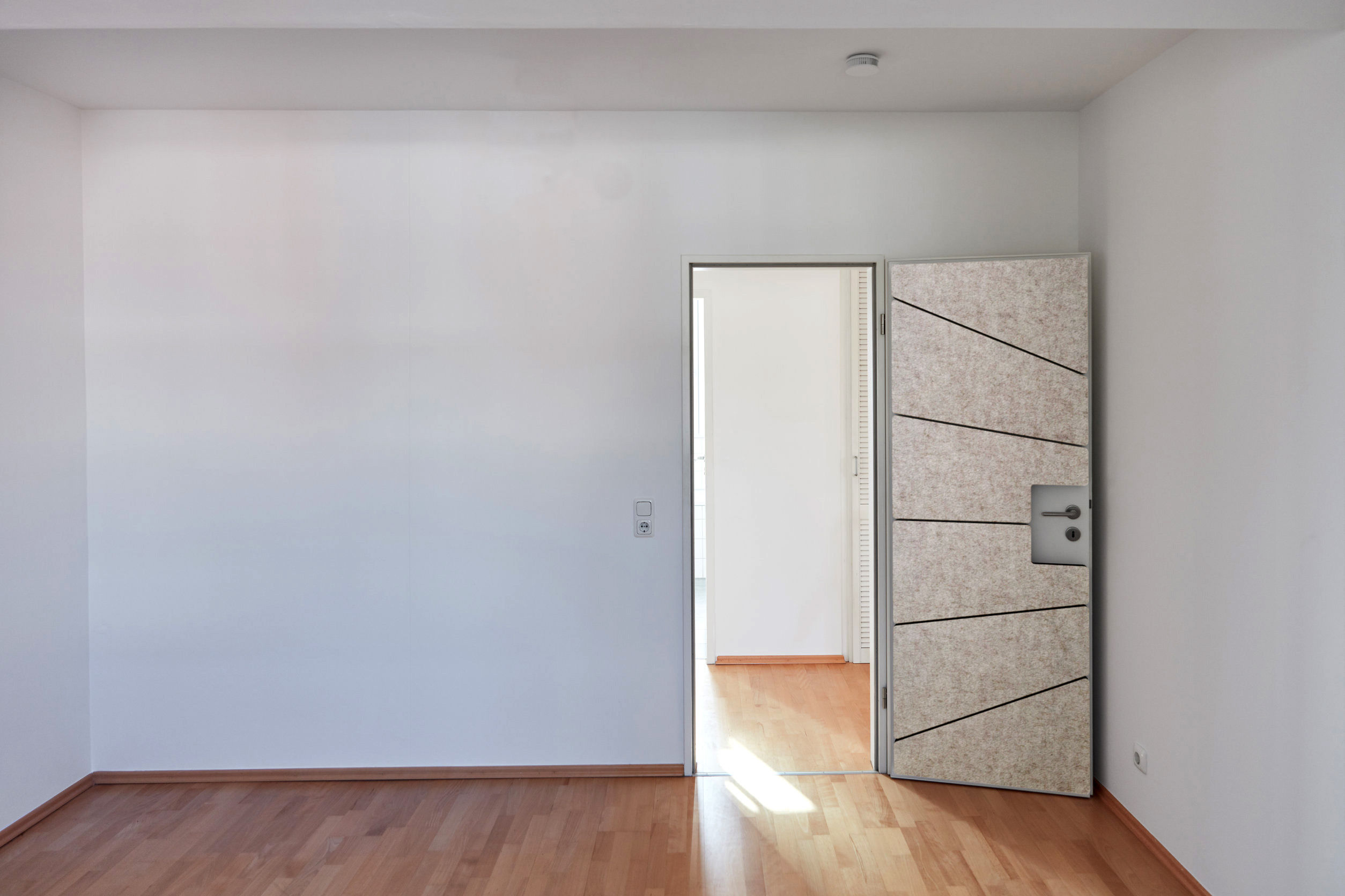 A living room with a door, white walls and parquet flooring, soni PORTA door insulation is applied to the door The door insulation is not full-surface, but consists of 6 individual elements with an attractive felt surface in anthracite, which fit exactly